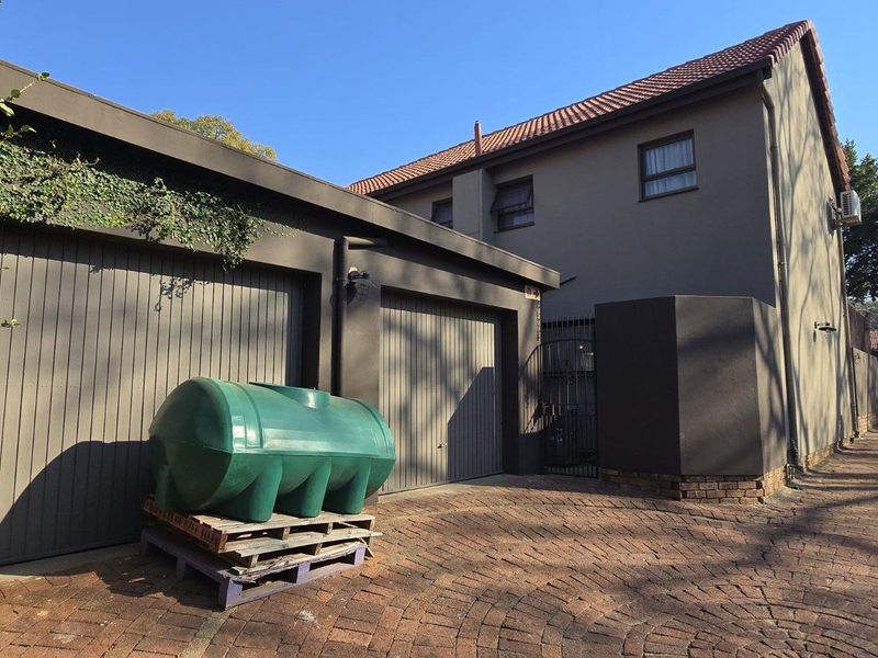 Exterior view of a townhouse featuring a double garage, paved driveway, and secure gated access.