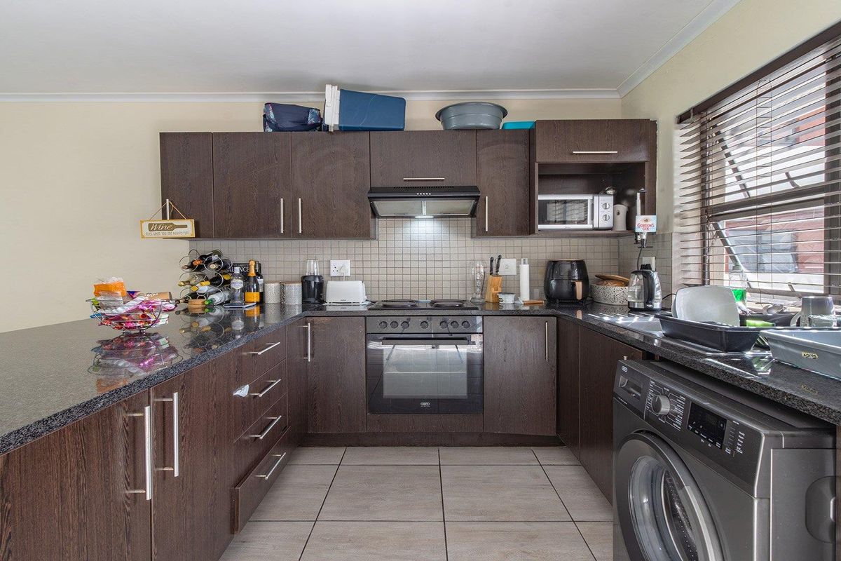 A functional kitchen featuring dark wood cabinetry, granite countertops, a built-in oven with extractor fan, and tiled flooring with integrated laundry space.