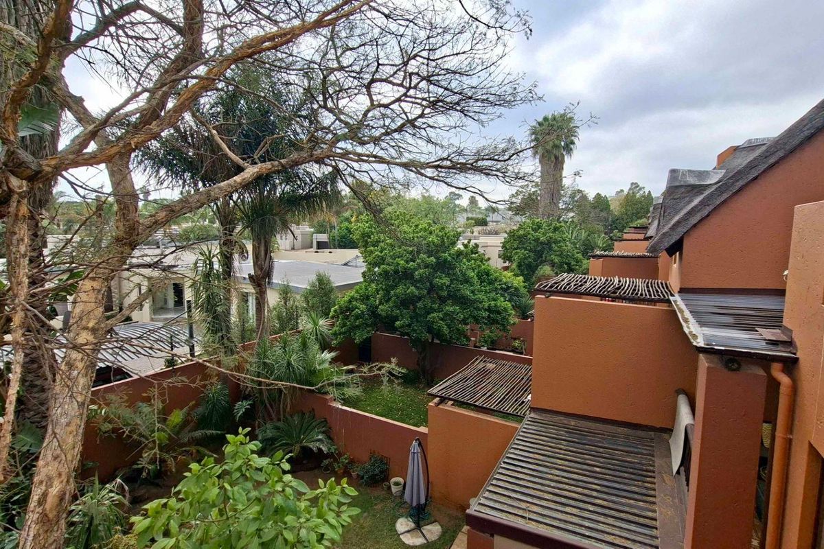 An elevated view of the rear exterior of the apartment complex, featuring a private garden area, terraced levels, and traditional thatched roofing.