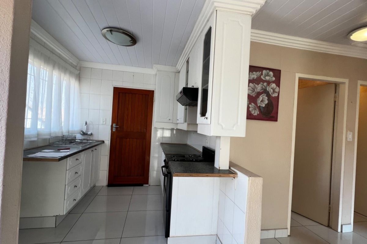 A functional kitchen featuring white cabinetry, tiled splashbacks, built-in oven and hob, and tiled flooring with direct access to an adjacent hallway.