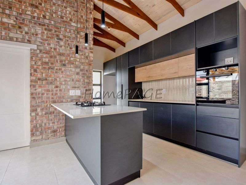 Modern kitchen featuring exposed brick walls, timber ceiling beams, a central island with stone countertops, and sleek dark cabinetry with integrated appliances.