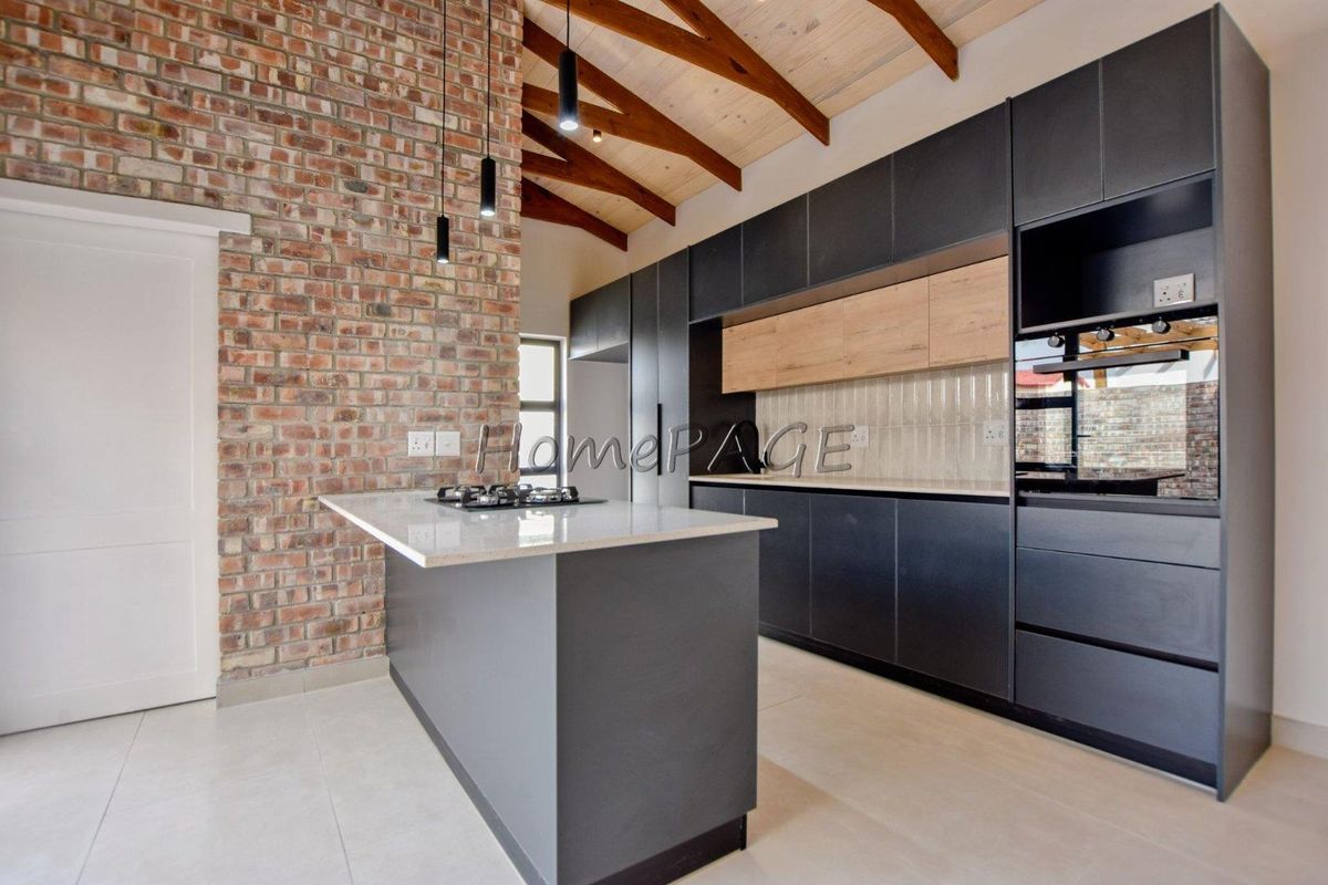 Modern kitchen featuring exposed brick walls, timber ceiling beams, a central island with stone countertops, and sleek dark cabinetry with integrated appliances.