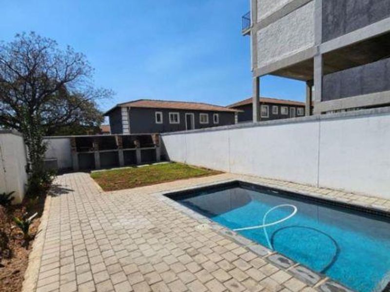 Outdoor pool area featuring a paved patio, swimming pool, and built-in braai facilities within a secure complex setting.