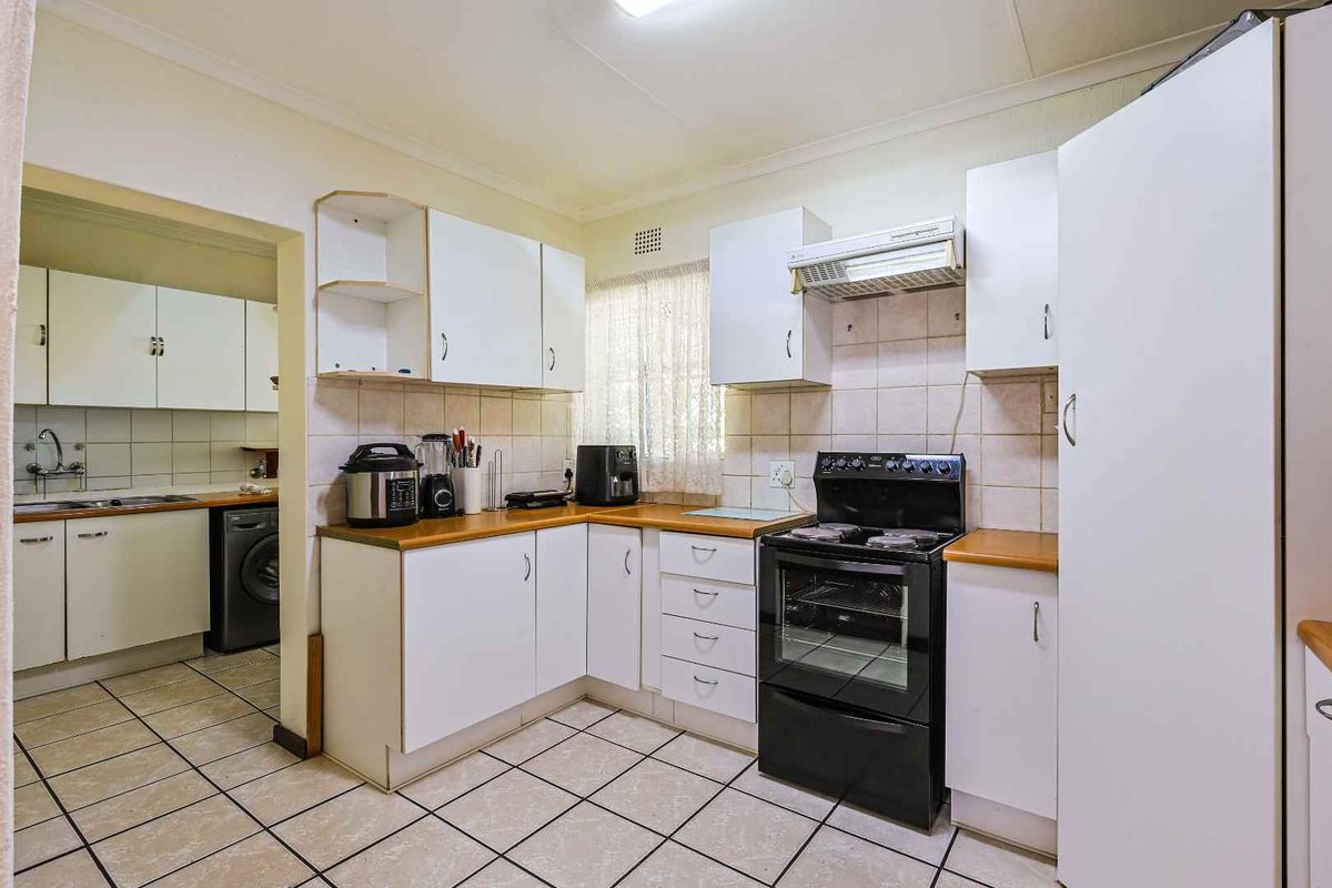 Functional kitchen featuring white cabinetry, wood-look laminate countertops, tiled flooring, and a built-in oven with extractor fan, with an adjacent scullery area.