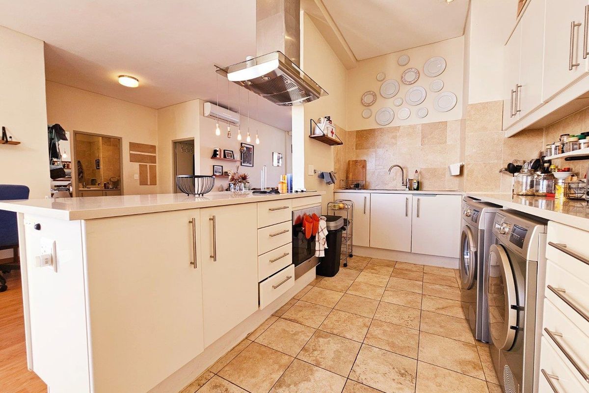 Modern kitchen featuring a central island, stone countertops, stainless steel extractor fan, built-in oven, and tiled flooring with integrated laundry appliance space.