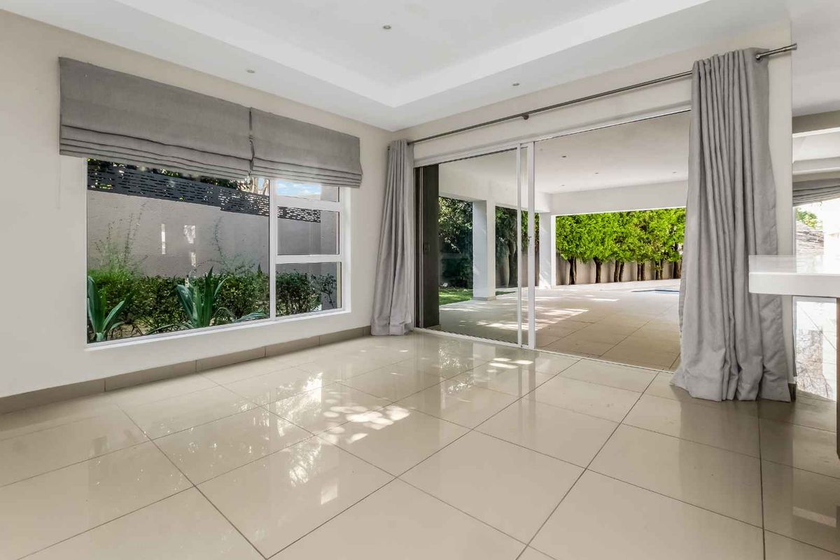 Bright living area featuring large porcelain floor tiles, recessed ceiling lighting, and expansive sliding glass doors opening onto a covered patio and garden.