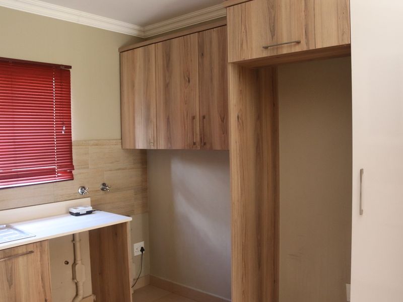 A functional laundry area featuring built-in wood-finish cabinetry, tiled splashback, and dedicated plumbing connections for appliances.