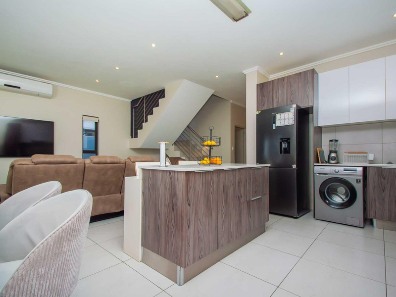 Modern open-plan living area featuring a contemporary kitchen with island, tiled flooring, and an integrated staircase leading to the upper level.