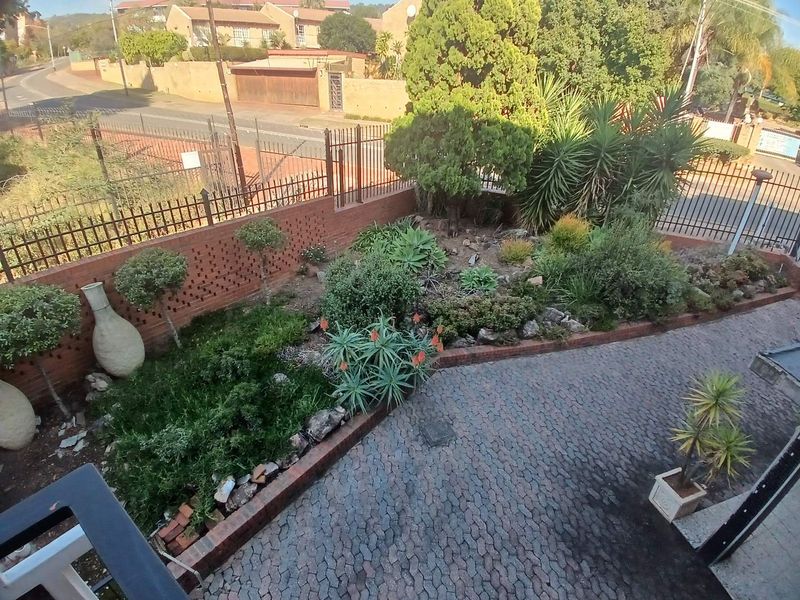 An elevated view of a landscaped garden featuring established shrubs, aloe plants, and cobblestone paving enclosed by a brick boundary wall and metal fencing.
