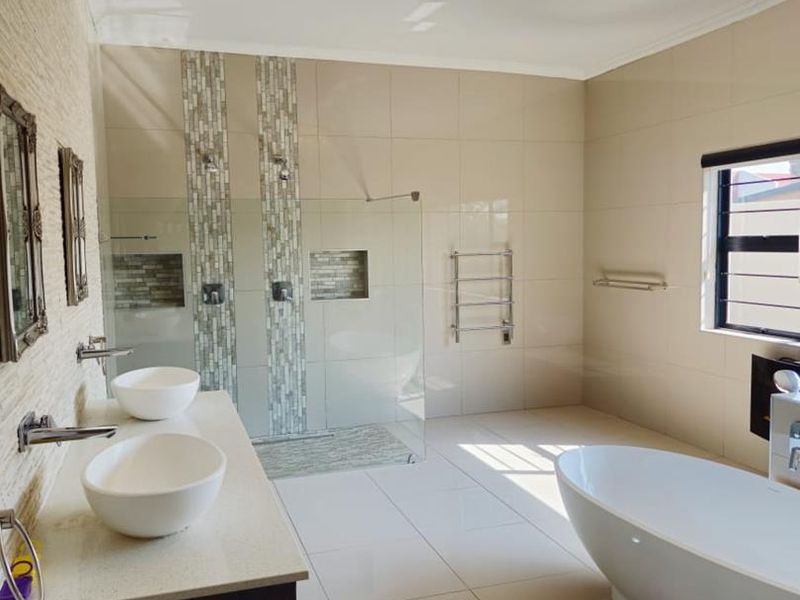 Modern, spacious bathroom featuring a double vanity, large walk-in shower with mosaic accents, a freestanding bathtub, and elegant crystal lighting.