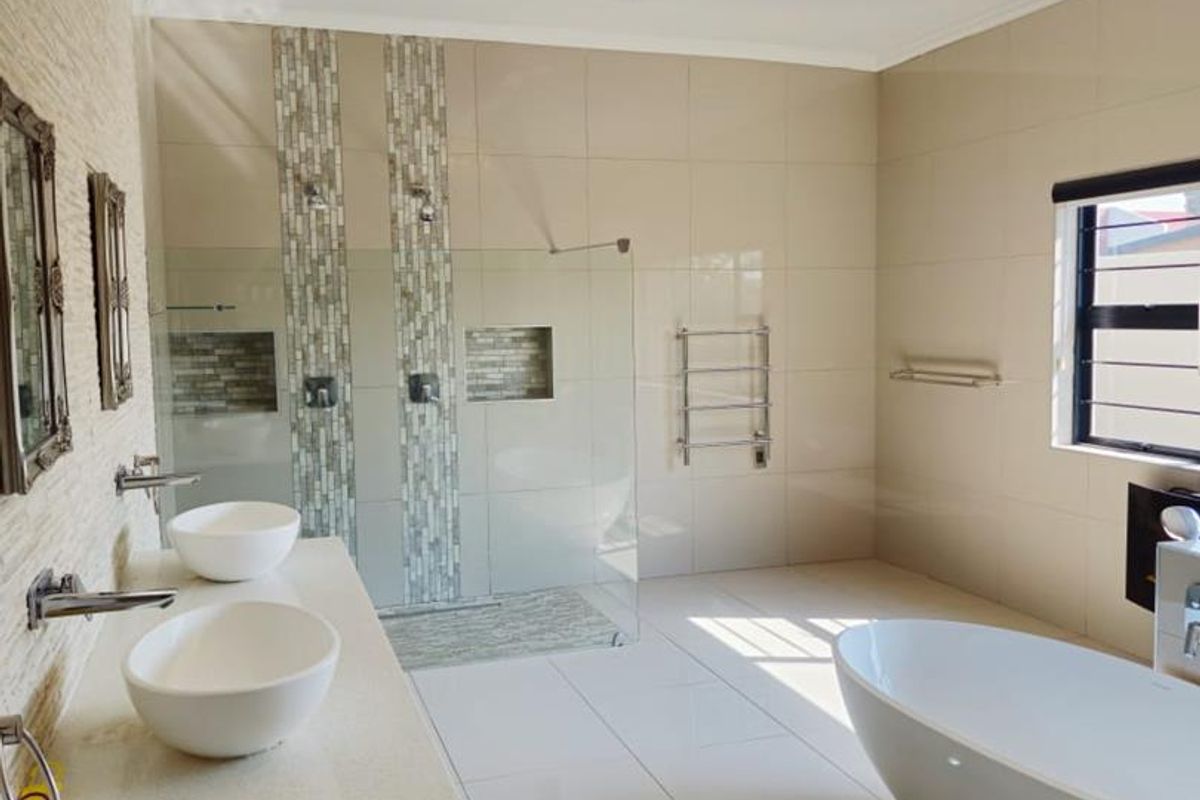 Modern, spacious bathroom featuring a double vanity, large walk-in shower with mosaic accents, a freestanding bathtub, and elegant crystal lighting.