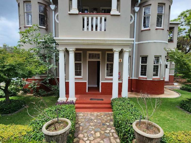 A well-maintained front facade of a multi-story residence featuring classic columns, a balcony, and a stone pathway leading to the entrance.