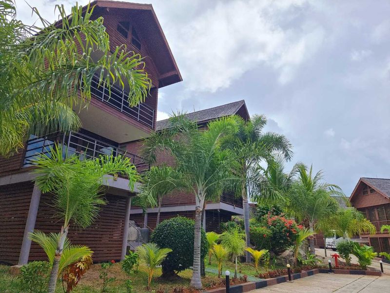 Exterior view of multi-story timber-clad commercial buildings featuring balconies, metal railings, and landscaped tropical garden surroundings.