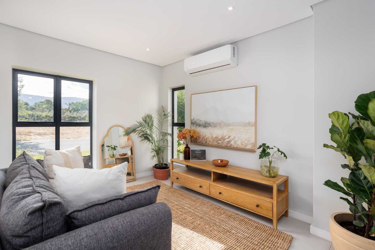 A bright and modern living room featuring large aluminium-framed windows, recessed downlighting, and a wall-mounted split-system air conditioning unit.