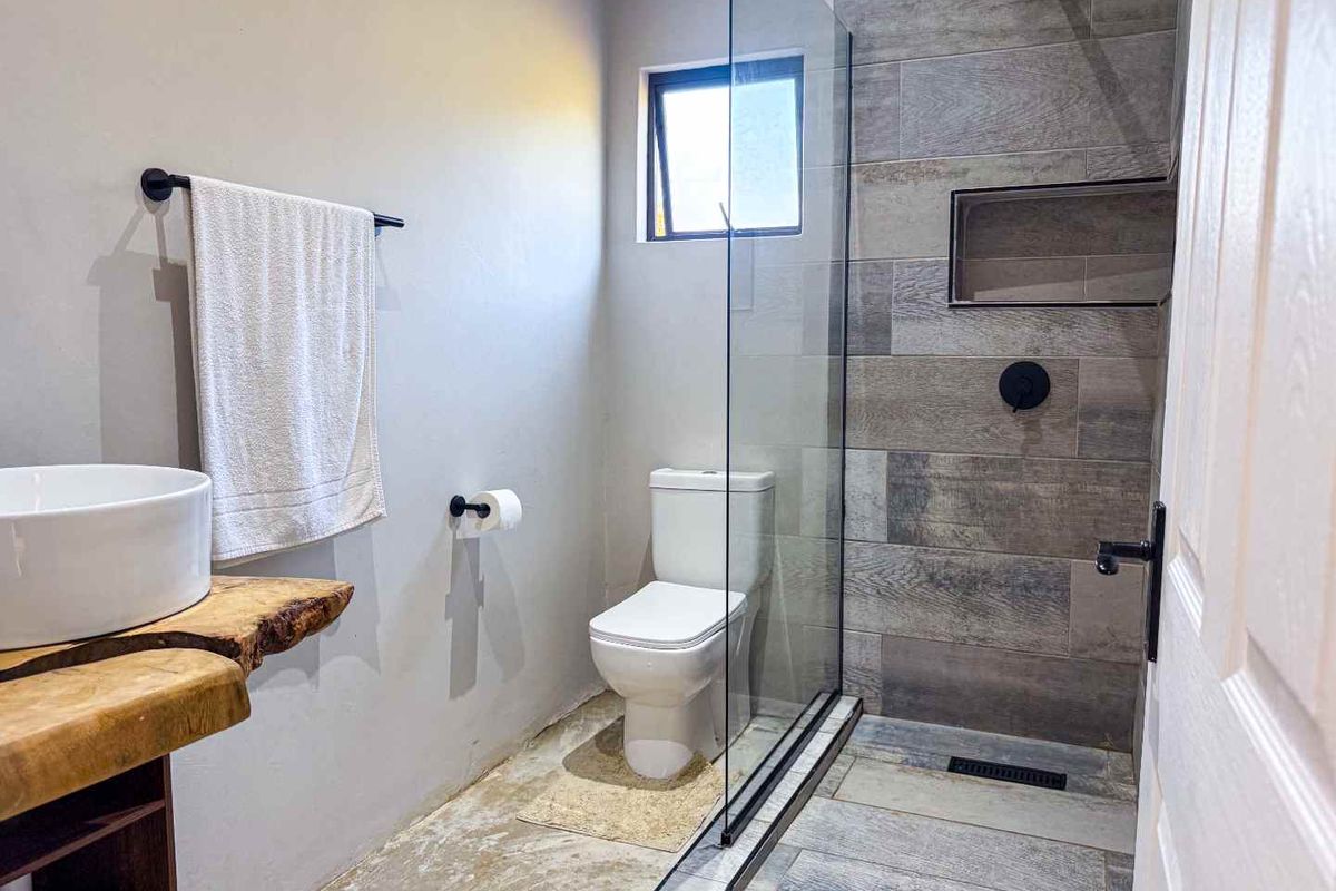 Modern bathroom featuring a walk-in shower with wood-look tile, glass enclosure, wall-mounted toilet, and a unique live-edge timber vanity top.