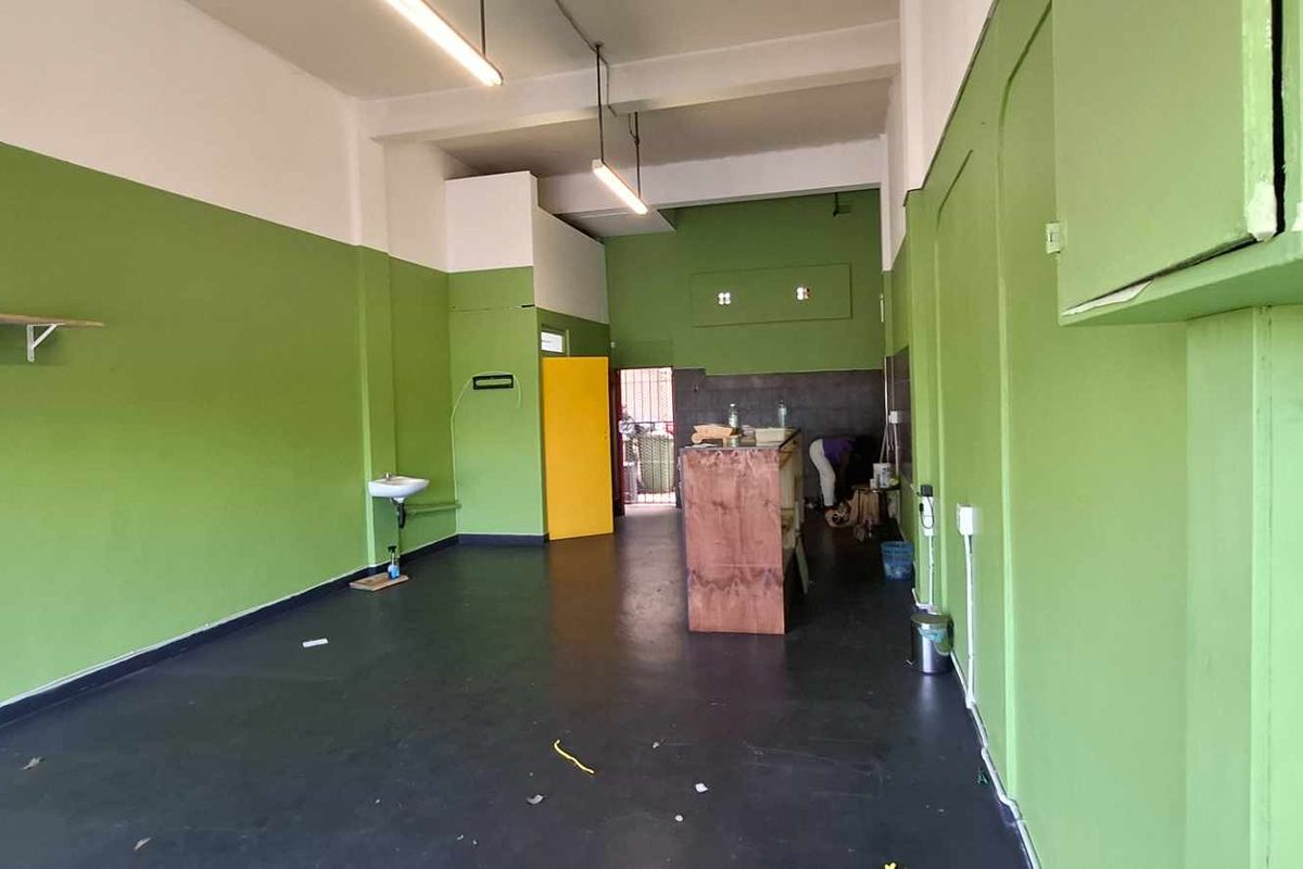 An open-plan commercial space featuring high ceilings, exposed beams, and a wall-mounted basin, offering a blank canvas for various business applications.