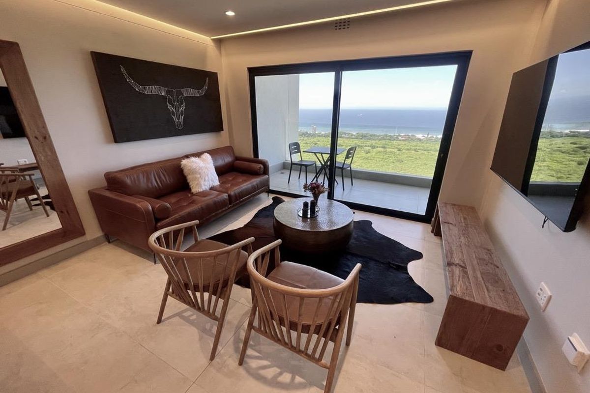 Modern living room featuring large sliding glass doors that open onto a balcony with expansive ocean and coastal views.