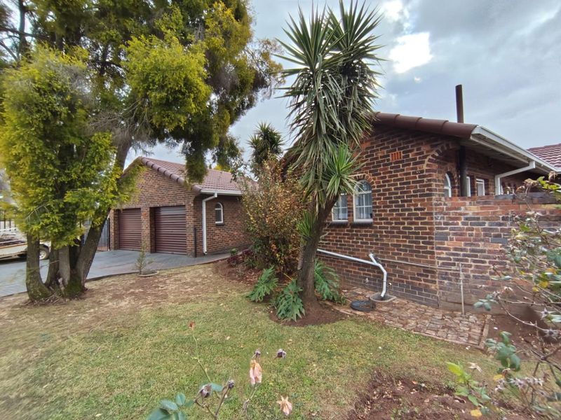 Rear view of a face brick house featuring a double garage with roller doors, arched windows, and a landscaped garden area.
