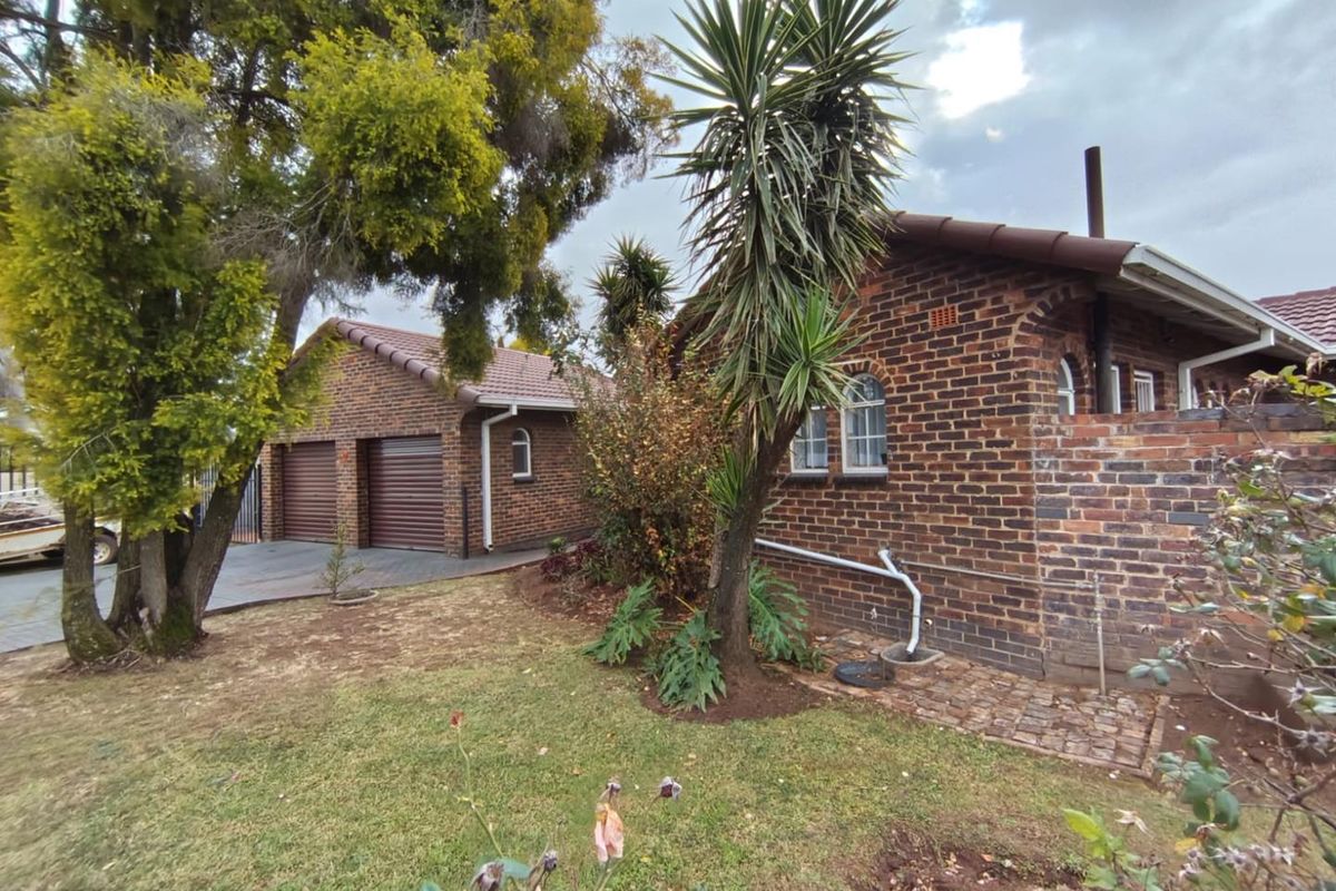 Rear view of a face brick house featuring a double garage with roller doors, arched windows, and a landscaped garden area.