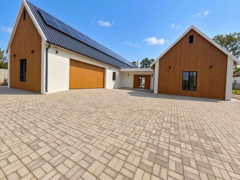 Modern architectural home featuring a large paved driveway, timber-clad facade, metal roofing with integrated solar panels, and a spacious garage.