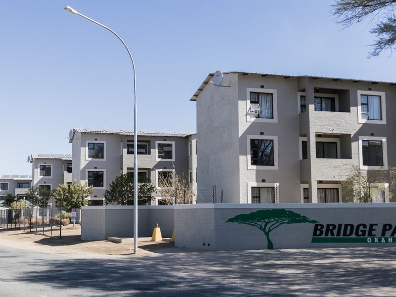 Exterior view of the Bridge Park apartment complex, featuring multi-story residential buildings with balconies, solar panels, and a secure perimeter wall.