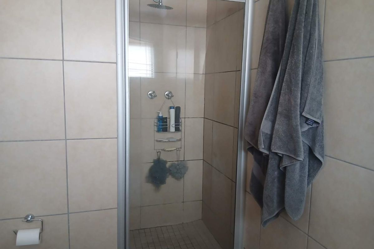 A functional bathroom featuring a tiled shower enclosure with a modern shower head and neutral wall tiling.