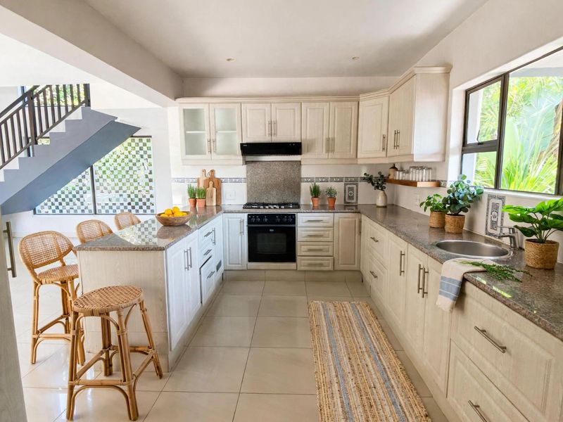 Modern kitchen featuring light wood cabinetry, granite countertops, built-in oven and gas hob, with an adjacent staircase and tiled flooring.