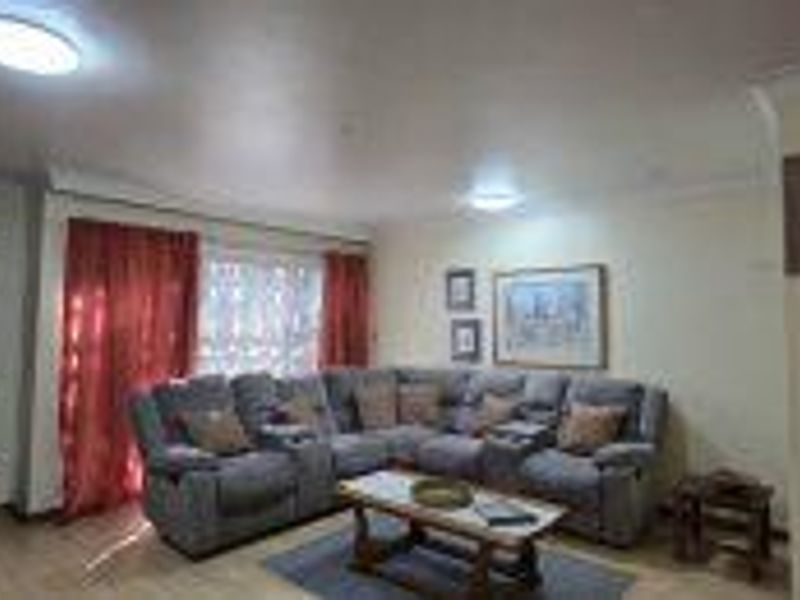 A spacious living room featuring laminate flooring, cove cornicing, and flush mount ceiling lights, providing a comfortable and functional area for relaxation.