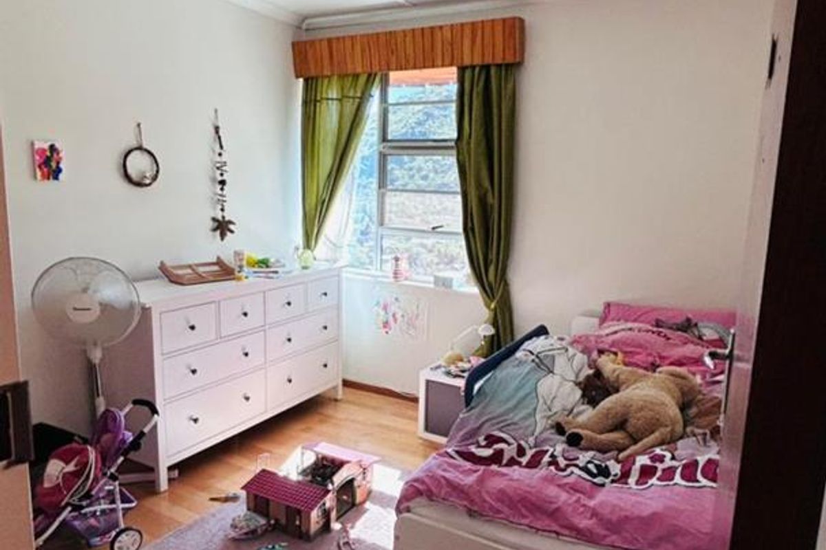 A functional bedroom featuring laminate flooring, a window with a wooden pelmet, and a ceiling-mounted light fixture.