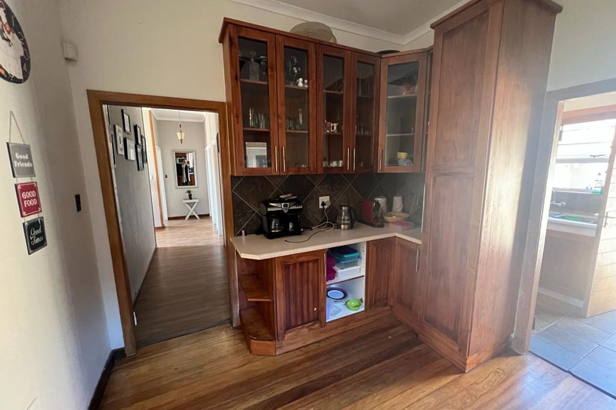 A kitchen corner featuring traditional wooden cabinetry, a tiled backsplash, and solid wood flooring, with an adjacent hallway and scullery area visible.