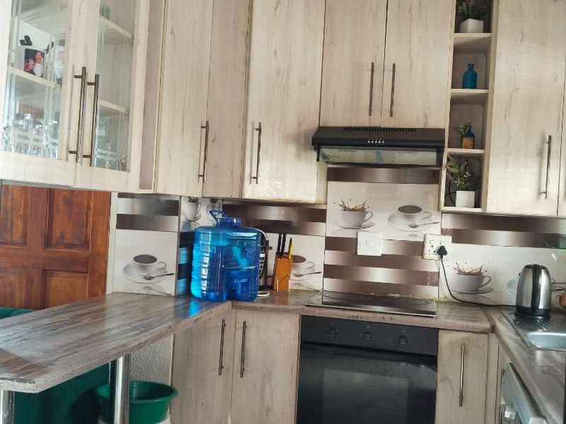 A functional kitchen featuring light wood-grain cabinetry, built-in oven and hob, extractor fan, and tiled flooring with a breakfast bar extension.