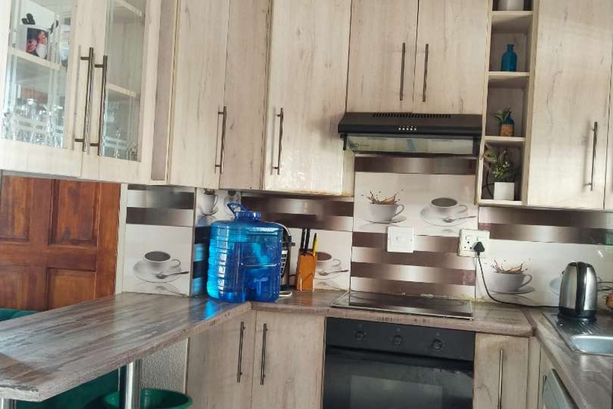 A functional kitchen featuring light wood-grain cabinetry, built-in oven and hob, extractor fan, and tiled flooring with a breakfast bar extension.