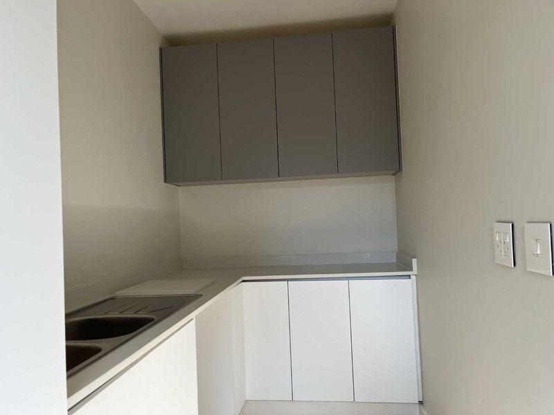 A clean, modern scullery featuring white lower cabinets, grey upper cabinets, a stainless steel sink, and stone countertops.