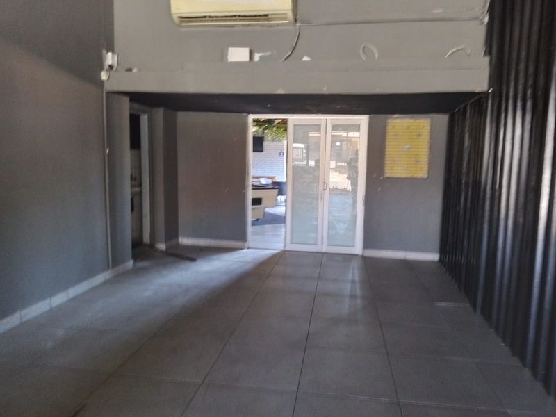 An open-plan retail space featuring tiled flooring, a split-system air conditioner, and glass sliding doors leading to an outdoor area.