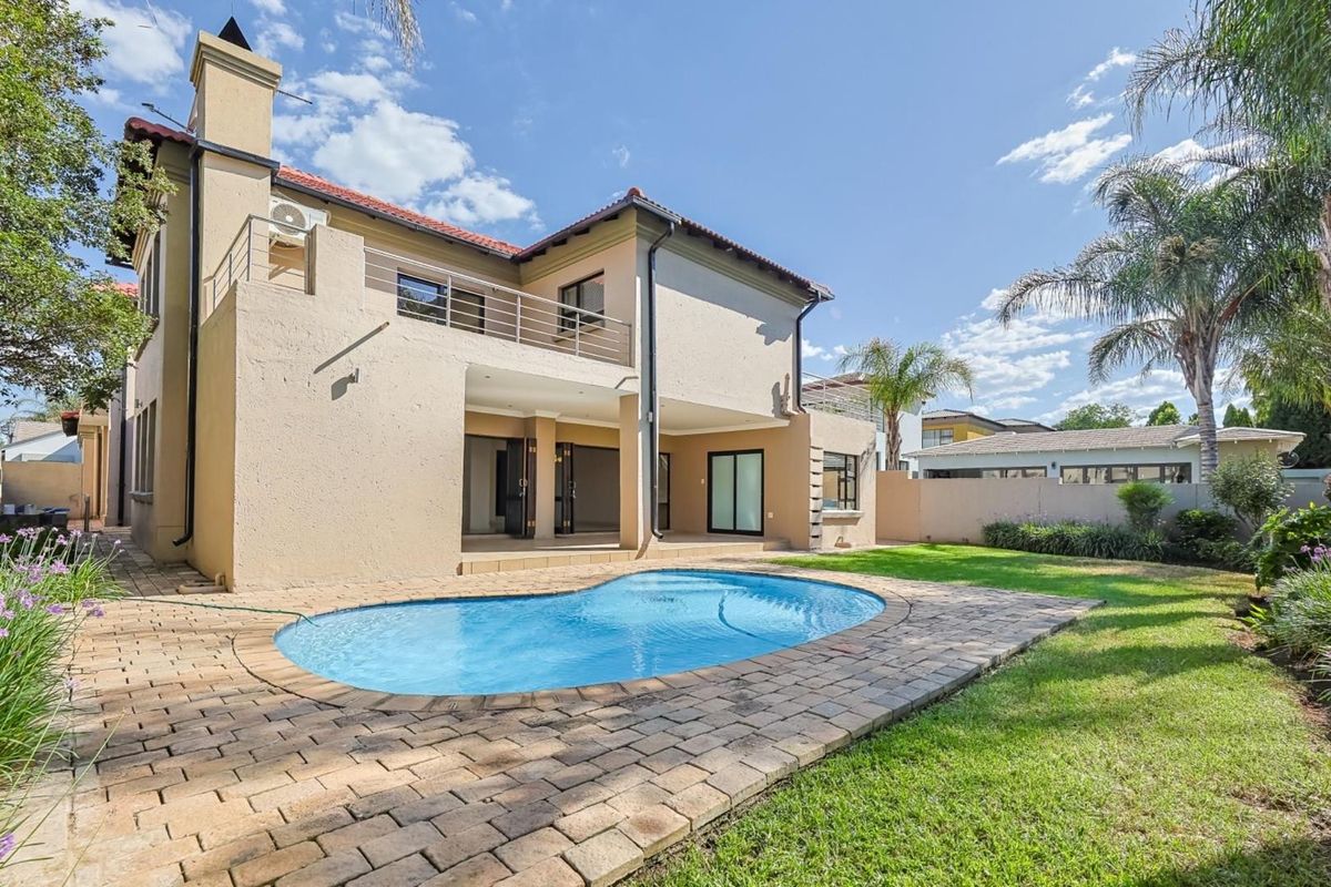Rear view of the house featuring a swimming pool, paved patio area, and a balcony accessible from the upper level.