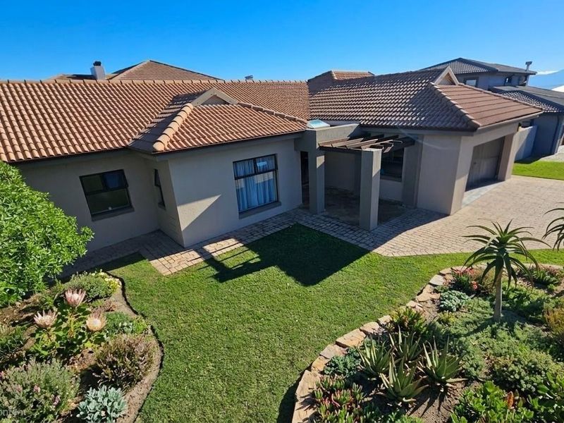 Elevated view of a well-maintained single-story residence featuring a tiled roof, paved driveway, integrated garage, and a landscaped front garden with a pergola entrance.