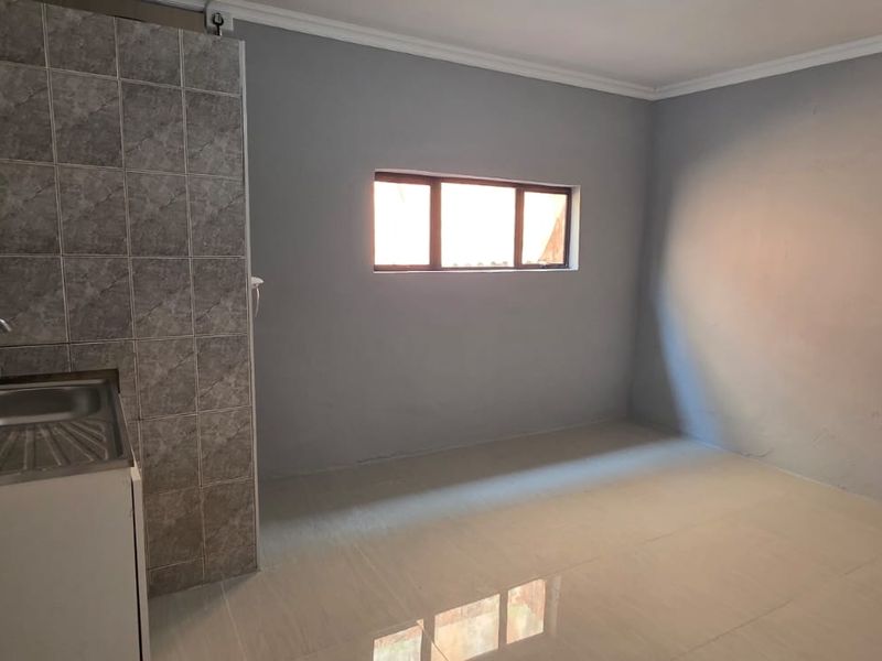 A compact, empty kitchen area featuring a stainless steel sink, tiled splashback, and neutral grey walls, ready for renovation or custom cabinetry installation.