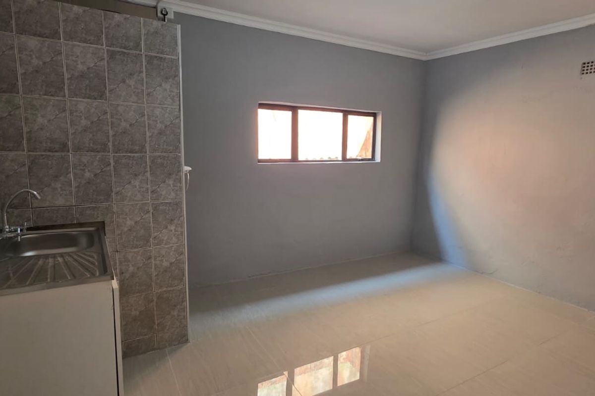 A compact, empty kitchen area featuring a stainless steel sink, tiled splashback, and neutral grey walls, ready for renovation or custom cabinetry installation.