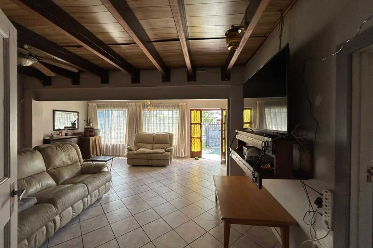 Spacious living room featuring exposed timber ceiling beams, tiled flooring, and direct access to the outdoor area through a sliding glass door.