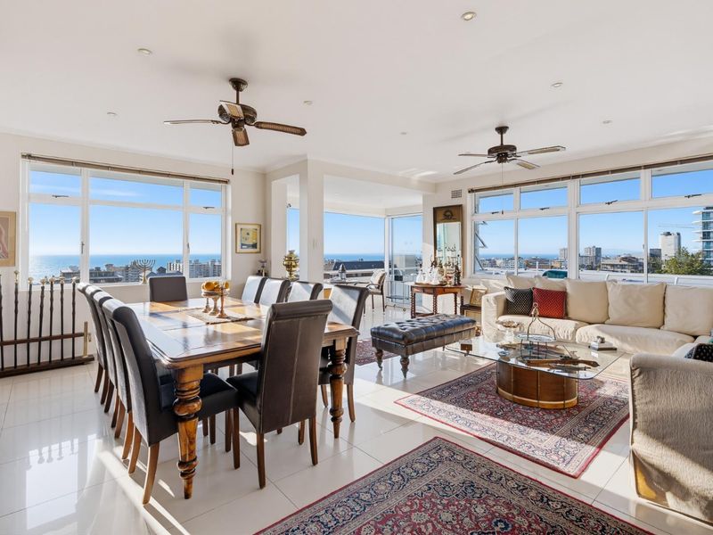 Spacious open-plan living and dining area featuring large windows with panoramic ocean and city views, tiled flooring, and ceiling fans.
