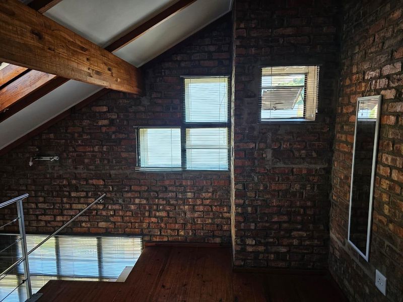 A characterful living space featuring exposed brick walls, vaulted ceilings with timber beams, polished wooden floors, and a modern stainless steel staircase balustrade.