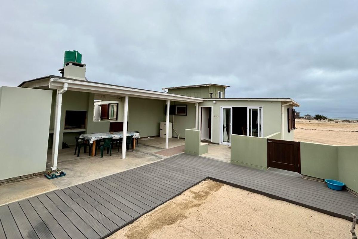 Rear view of the property featuring a covered patio area with a built-in braai, composite decking, and direct access to the sandy beach.