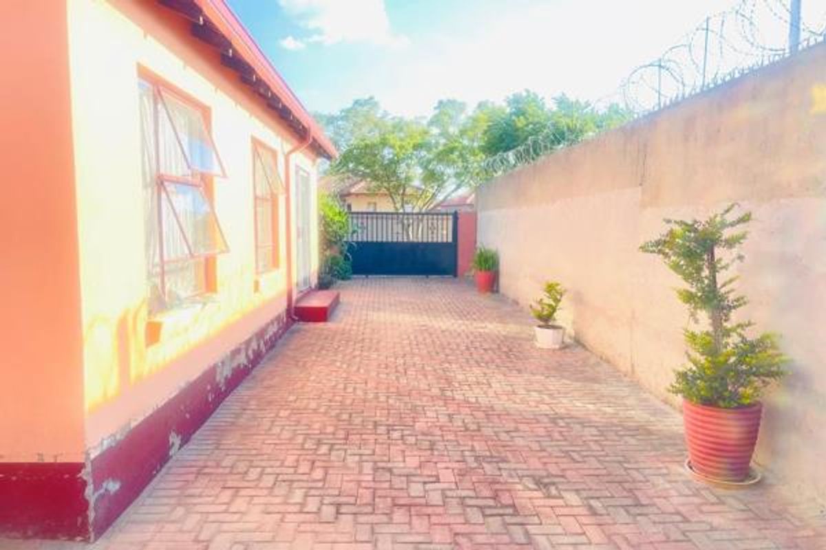 Side exterior view of the property featuring a paved driveway, perimeter wall with security wire, and access to the side entrance.