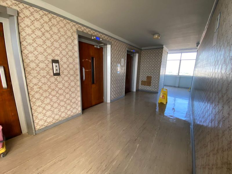 A communal apartment hallway featuring elevator access, patterned wallpaper, and vinyl flooring, currently showing signs of wear and maintenance needs.