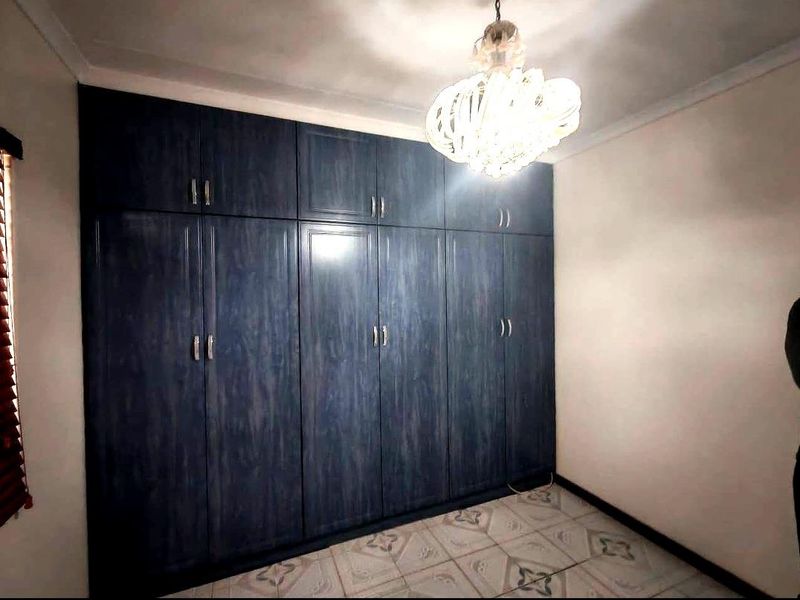 A bedroom featuring extensive dark wood-grain built-in cupboards, tiled flooring, and decorative ceiling lighting.