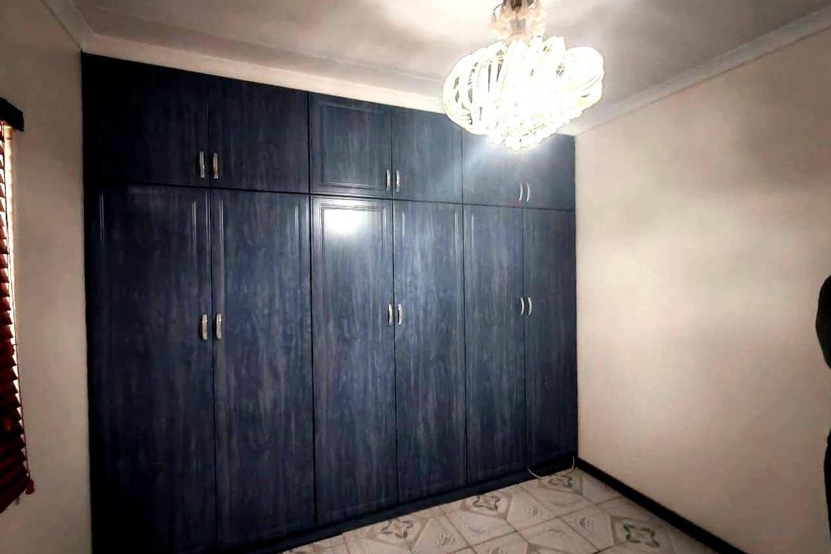 A bedroom featuring extensive dark wood-grain built-in cupboards, tiled flooring, and decorative ceiling lighting.
