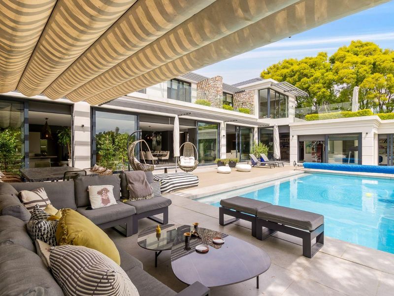 A luxurious outdoor entertainment area featuring a swimming pool, stone patio, retractable awning, and seamless indoor-outdoor flow through large sliding glass doors.