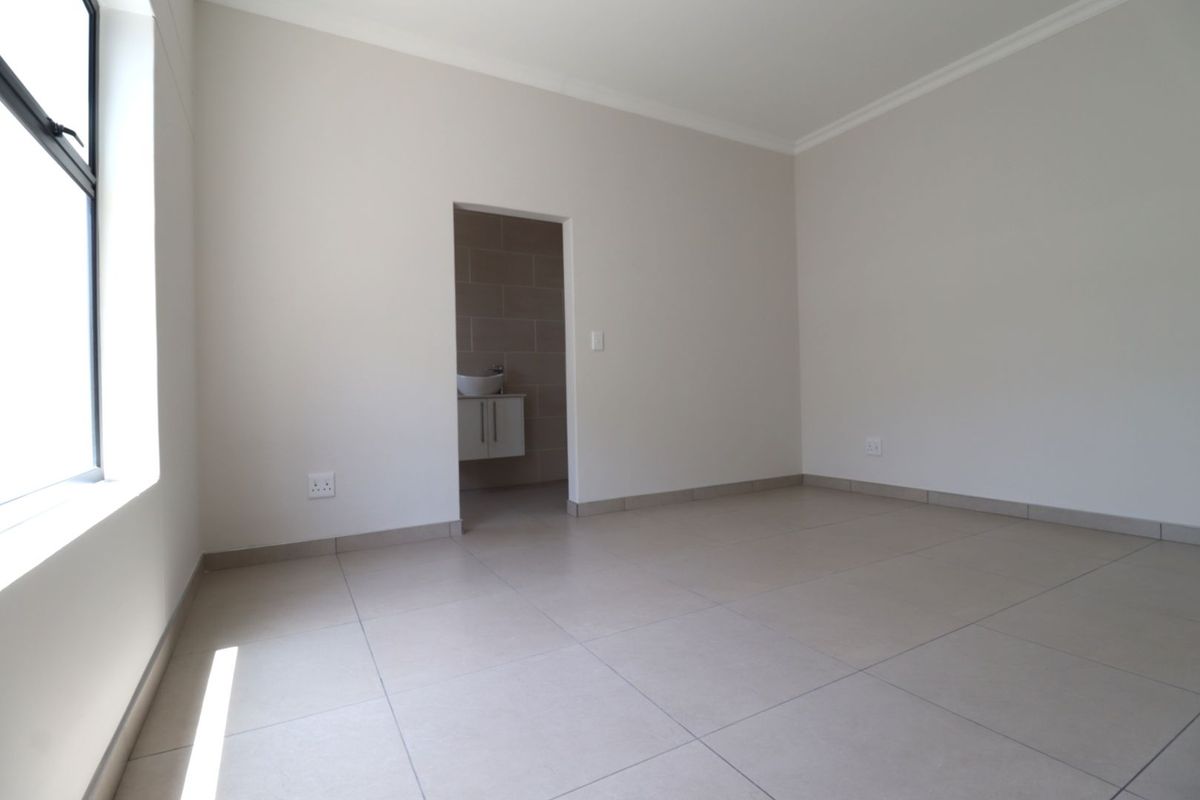 A bright, empty bedroom featuring neutral tiled flooring and a doorway leading to an en-suite bathroom with a vanity unit.