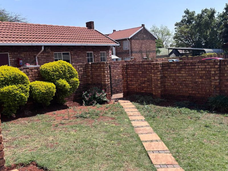 A private rear garden area featuring a face brick boundary wall, tiled roof structure, and a paved walkway leading to a gated entrance.