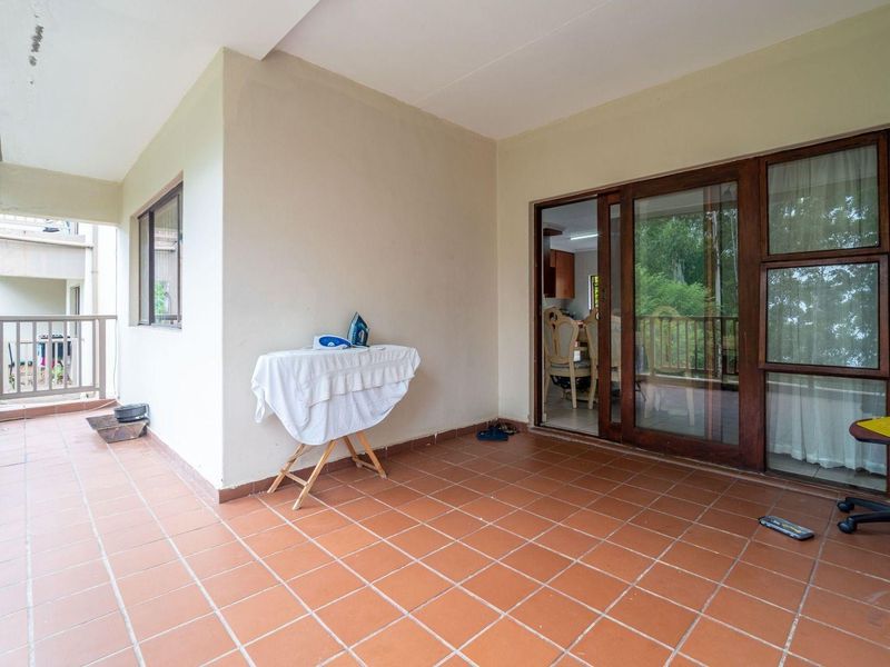 A covered patio area featuring terracotta floor tiles and sliding glass door access to the interior living space.